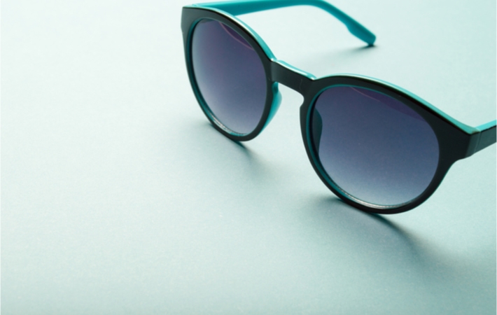 Pair of fashionable sunglasses with dark lenses sitting on a light teal background.