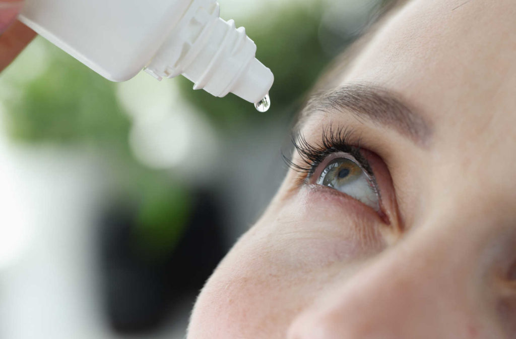 A woman putting an eye drop in her eye.