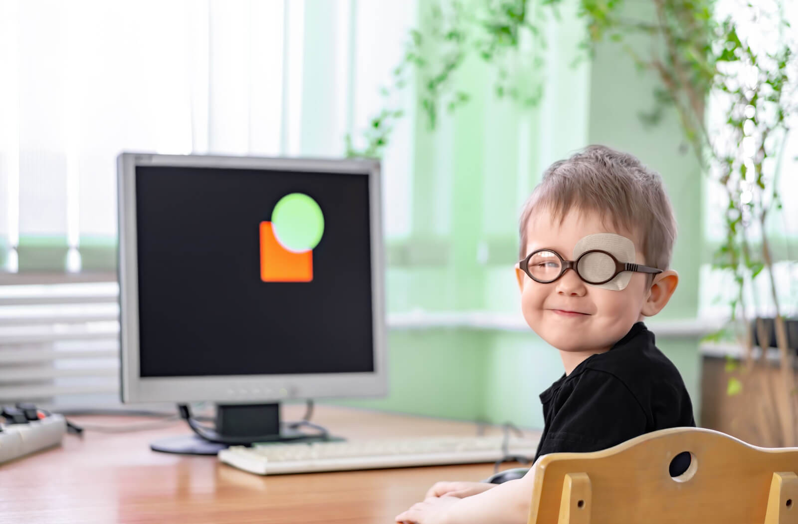 A boy with a patch on his eye sitting in front of a computer doing a vision exercise.