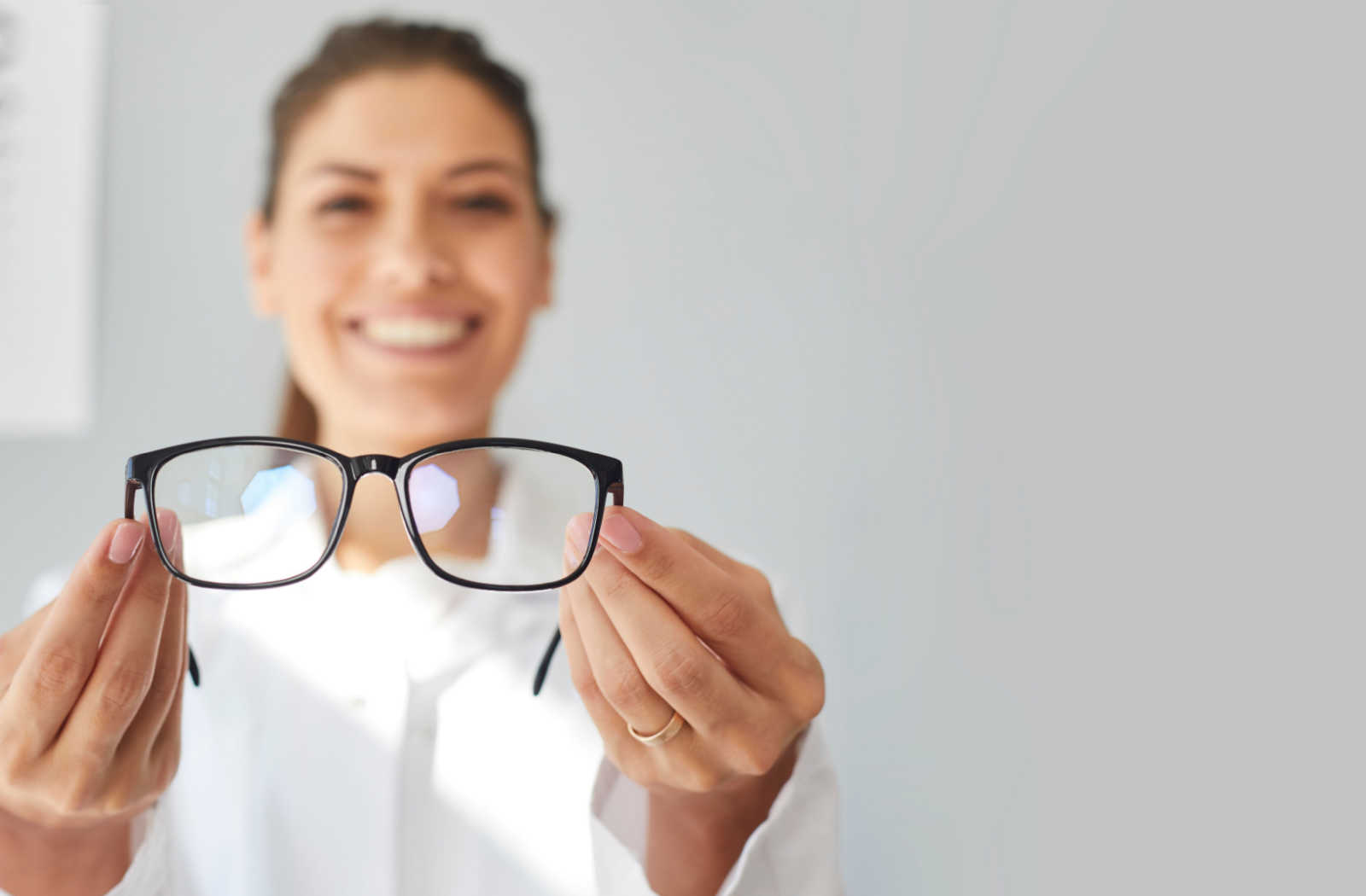 An optometrist holding a pair of prescription glasses as she smiles and looks directly at the camera.
