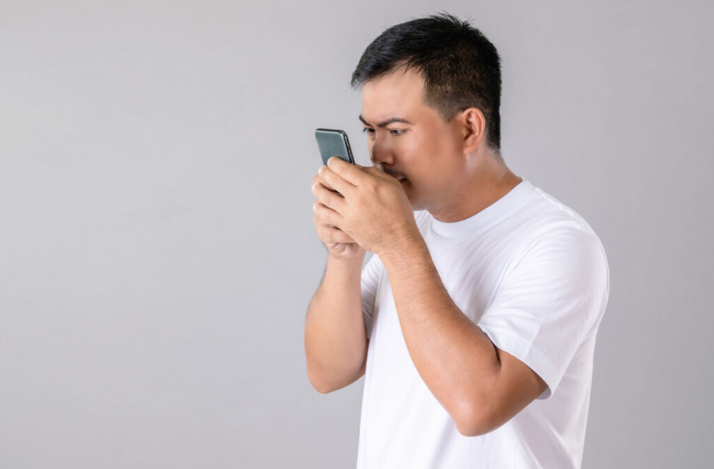 A man with nearsightedness holds his smartphone close to his eyes.
