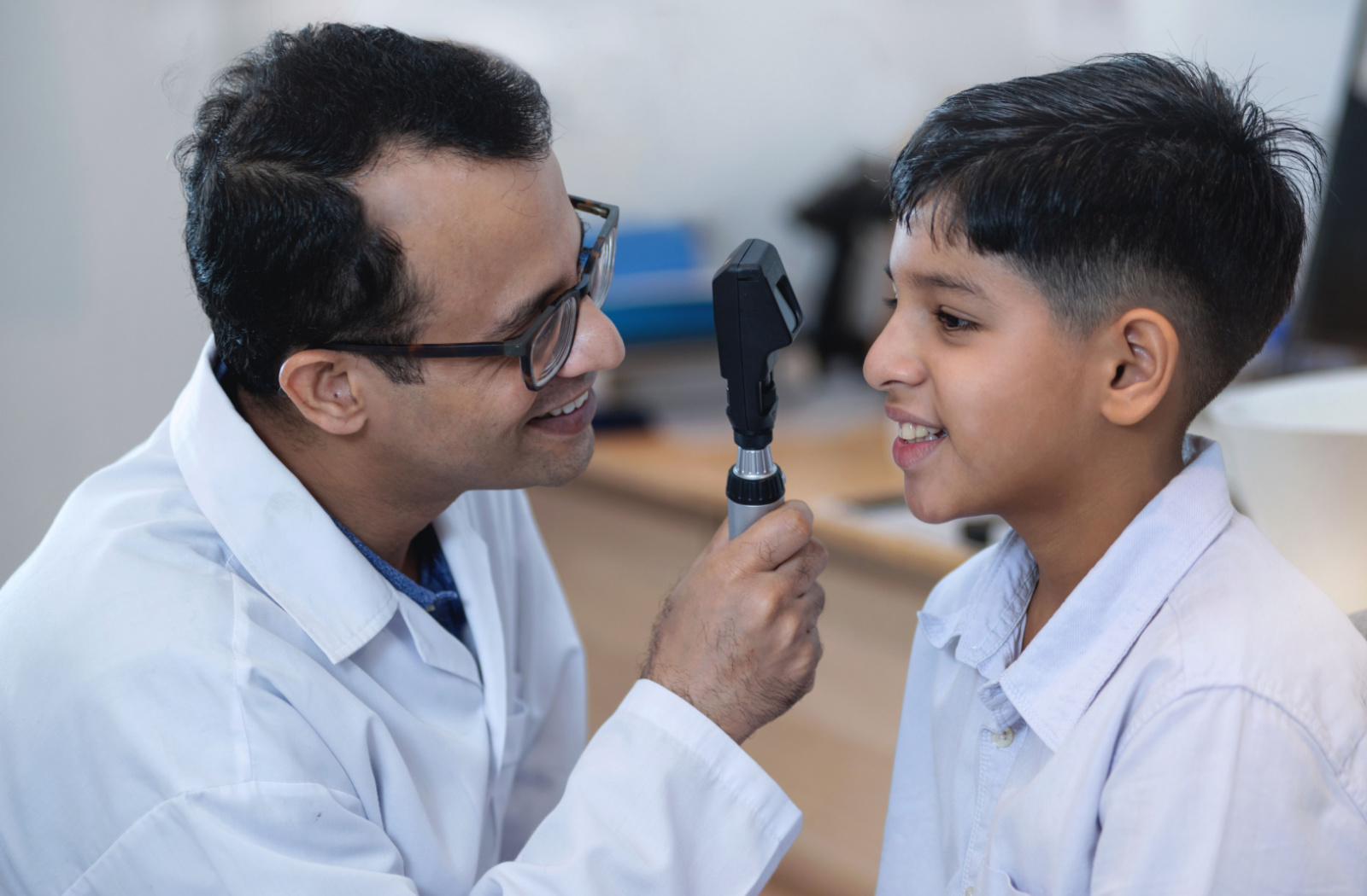 An optometrist smiling and conducting an eye exam on a child using a device that tests his vision.