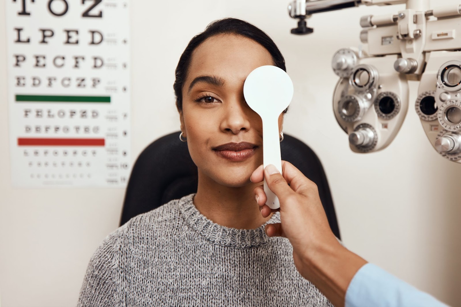 A woman in an optometrist's office with her left eye covered by a white paddle.