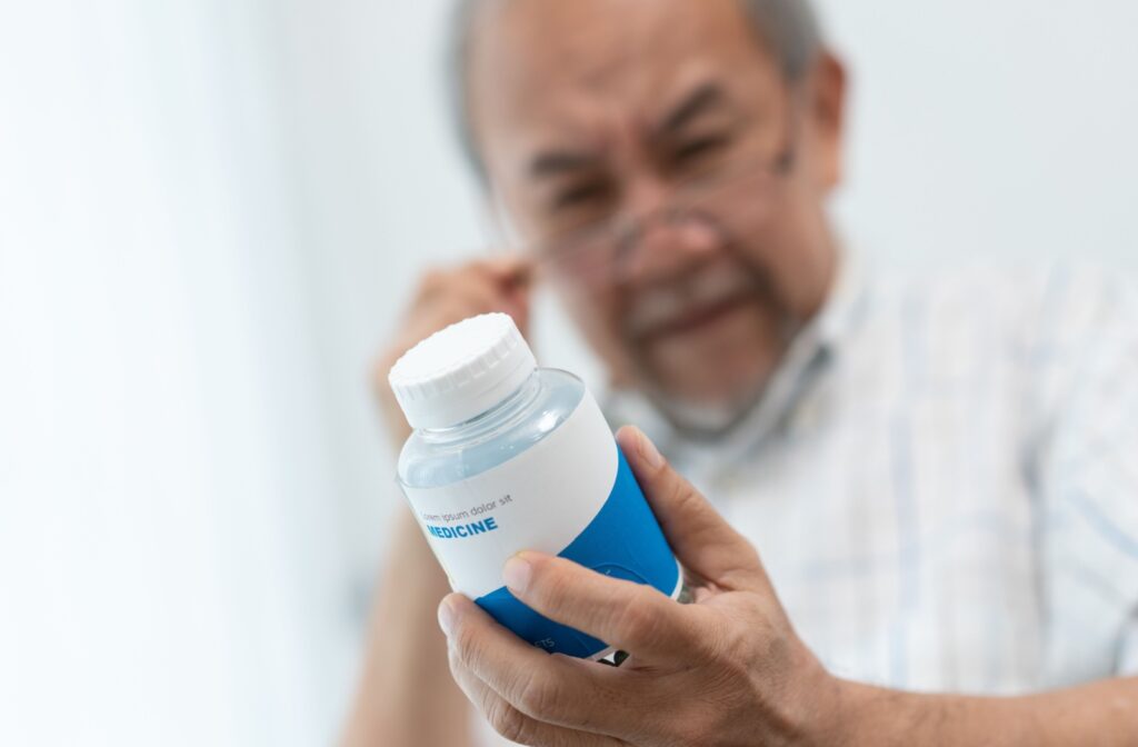 A mature Asian man having difficulties reading his medicine bottle with his glasses on.