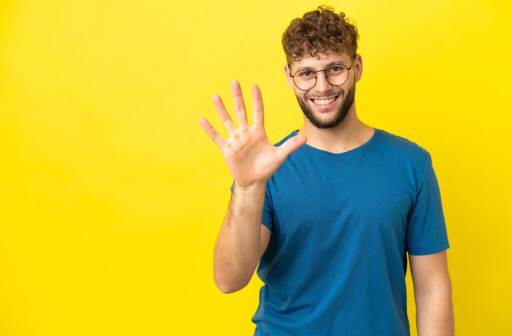 A happy patient with eyeglasses holding up 5 fingers.