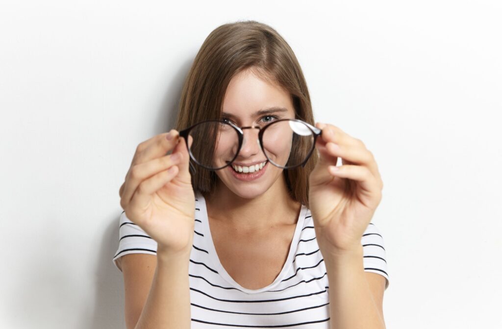 A person holds their glasses at a distance, delighted they no longer need them.