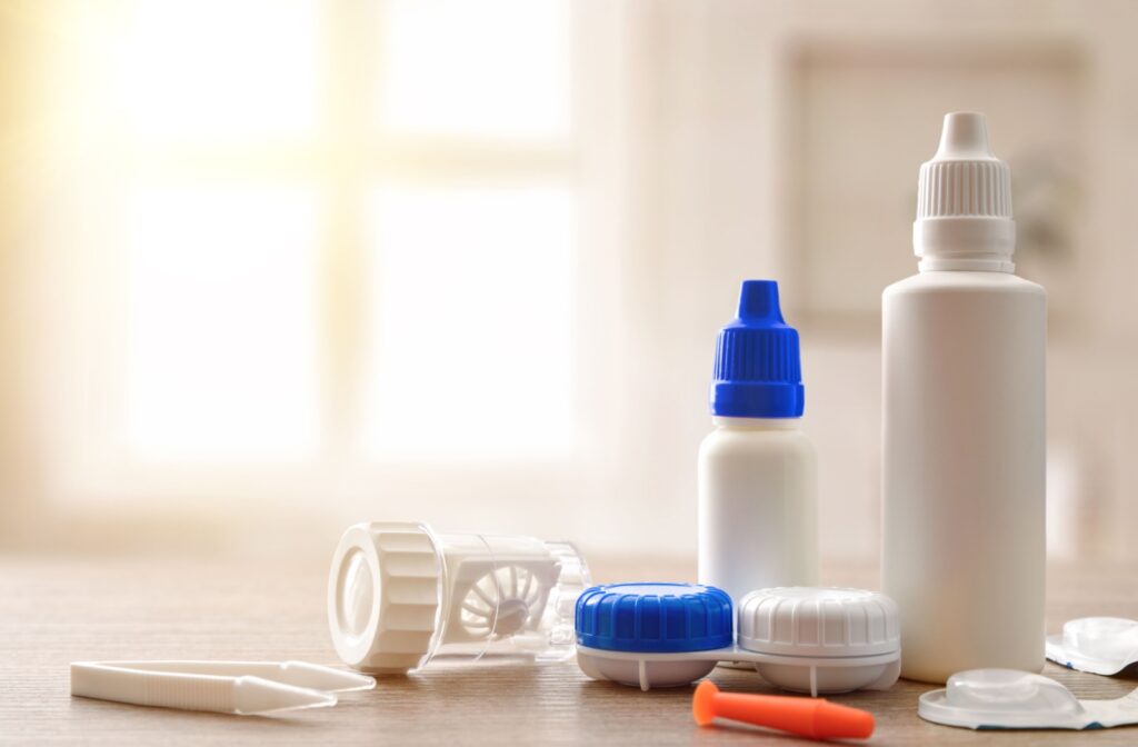A set of contact lens care supplies, including solution bottles, lens cases, and tweezers on a table.